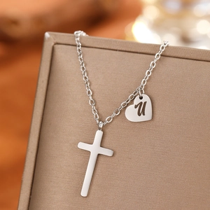 Close-up of silver stainless steel cross and heart pendant with letter U engraving