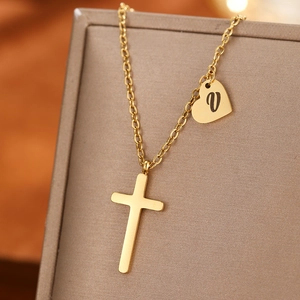Detail of gold cross and heart pendant necklace with letter V engraving on display box