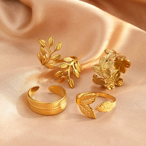 Detailed set of four golden stainless steel rings with floral and leaf designs on silk