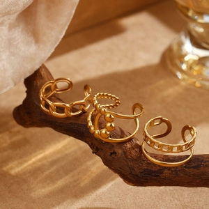 Detailed view of three gold braided Cuban chain rings on a textured wooden stand