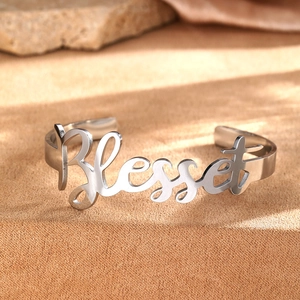 Detailed view of silver stainless steel open bangle with Blessed lettering on sand background