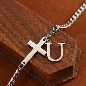Detailed macro of stainless steel curb chain with cross and letter U charm on wood