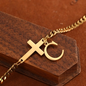 Detail of gold-plated Cuban chain anklet featuring cross and letter C charms on wood