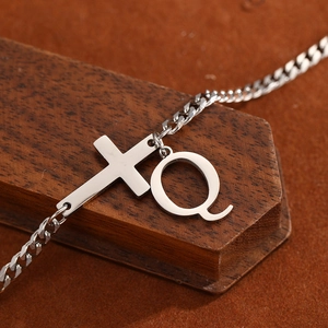 Macro shot of silver stainless steel anklet with a horizontal cross and letter Q charm