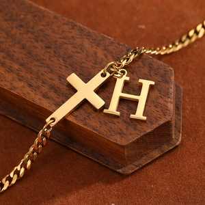 Detailed close-up of gold stainless steel cross and H letter pendant on a Cuban chain