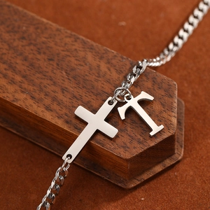 Detailed close-up of stainless steel cross and letter T charms on a silver anklet chain