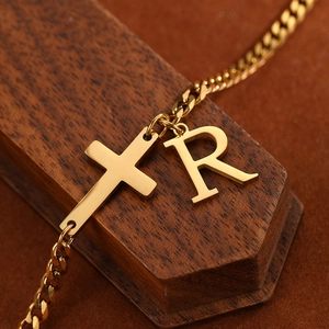Macro detail of gold curb chain anklet featuring polished cross and letter R pendant
