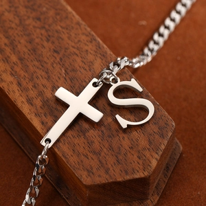 Macro shot of silver stainless steel Cuban chain anklet with cross and letter S pendant