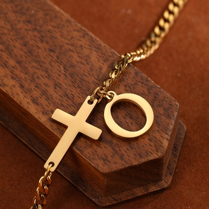 Detail of gold stainless steel anklet with cross and alphabet charm on textured wood