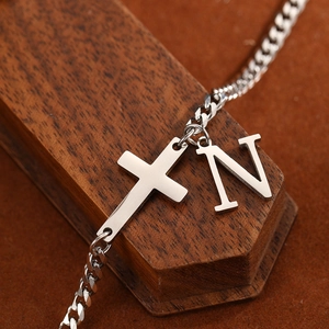 Detail of silver stainless steel anklet with cross and letter N pendant on wood