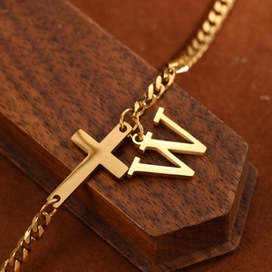Detail of a golden stainless steel anklet with a cross and a letter W pendant