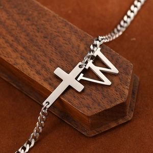 Macro shot of silver stainless steel cross and W letter charm on classic cuban chain anklet