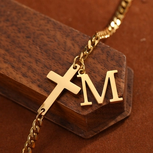 Detailed close-up of golden stainless steel curb chain with cross and 'M' letter pendant