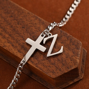 Macro detail of stainless steel anklet featuring cross and letter Z charms on cuban chain