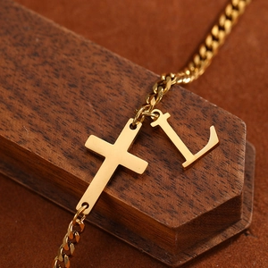 Macro shot of gold cross and letter L pendant on a polished Cuban chain anklet