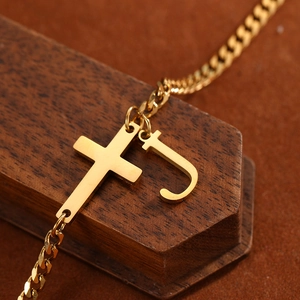 Detail of a gold stainless steel curb chain with a polished cross and letter J pendant