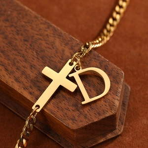 Macro shot of gold stainless steel anklet with letter D and cross charm on wood