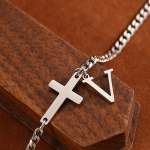 Detail of a silver stainless steel cross and V-letter pendant on a metal anklet