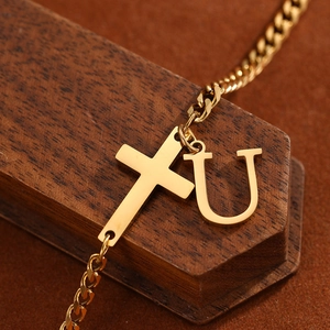Detail of a gold-plated Cuban link anklet with a cross and letter U charm on wood