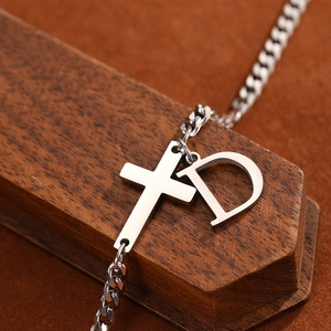Silver stainless steel anklet with cross and D-letter charms on a wooden surface