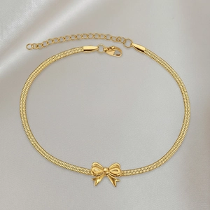 Detailed view of gold snake chain bracelet featuring 3D bow charm on champagne silk background