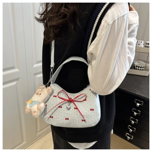 Close-up of light blue crescent bag with red bows and a plush bear charm on strap