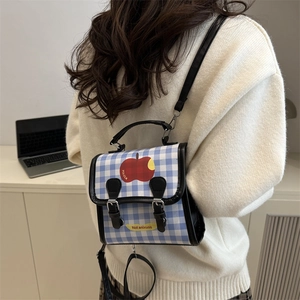 Blue and white plaid backpack with red apple graphic shown worn on a model's back
