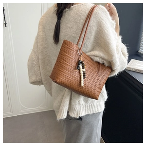 Brown woven tote bag with beaded tassel detail worn by a model in a minimalist setting