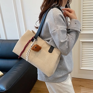 Retro canvas tote bag with black leather straps and teddy bear charm on model's shoulder
