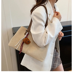 Detail of canvas tote bag with brown leather straps and cute plush bear charm accessory