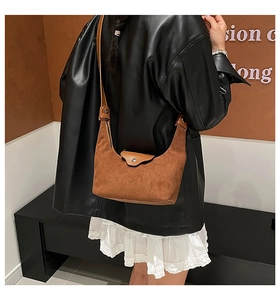 Close-up of brown suede shoulder bag with smooth leather strap and metal button detail