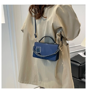 Détail du sac bandoulière bleu marine avec boucle dorée et chaîne sur un trench-coat