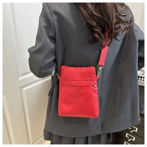 Close-up of red lychee textured crossbody bag with fabric strap on grey blazer