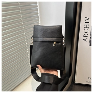 Detail of black lychee-grain vertical square bag with gold zipper and wide strap