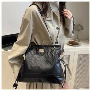 Detail of black quilted leather tote bag featuring golden chain strap and side drawstrings