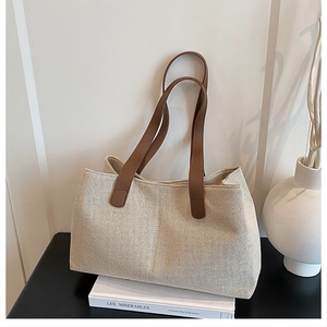 Close-up of large canvas tote bag with brown leather handles on minimalist background