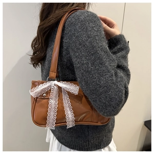 Close-up of brown faux leather underarm bag with decorative white lace bow detail