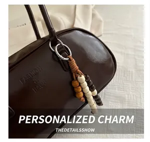 Detail of dark brown glossy handbag with embossed lettering and retro wooden bead charm