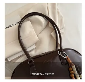 Detail of dark brown polished PU Boston bag with FASHION logo and beaded pendant