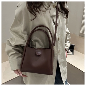 Dark brown leather bucket bag shown as a crossbody on model in a minimalist urban setting