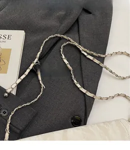 Detail of the woven gold metal chain strap on a white embossed leather crossbody bag