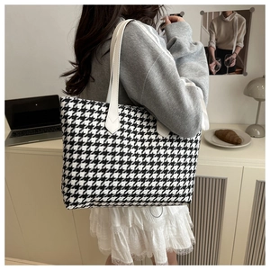 Model carrying a black and white houndstooth tote bag with white leather straps in a home setting