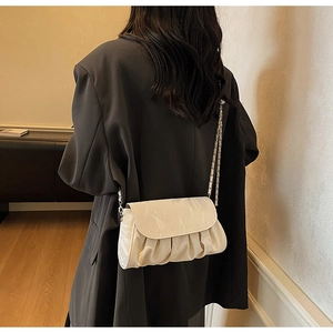 Détail du sac plissé crème avec bandoulière chaîne argentée sur un mannequin en blazer gris