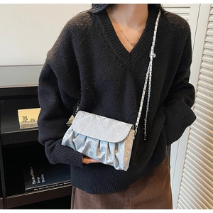 Detail of silver metallic wrinkled shoulder bag with chain strap worn by a model