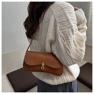 Brown leather shoulder bag with gold U-shaped buckle shown on a knit sweater outfit