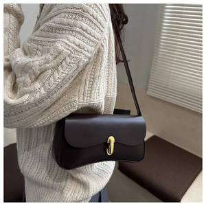 Detail of deep brown leather shoulder bag featuring a sleek gold oval buckle clasp