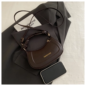Detail of dark brown crescent bag with woven handle and gold fashion lettering