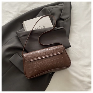 Detailed close-up of dark brown crocodile pattern underarm bag on grey suit
