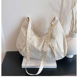 Detail of off-white dumpling bag with pleated texture and adjustable strap on a book