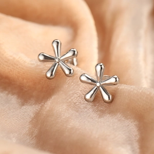 Elegant polished silver flower stud earrings on a beige velvet background